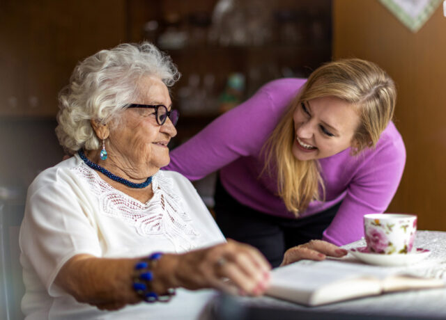 A lady in a pink jumper chatting to an elderly lady.