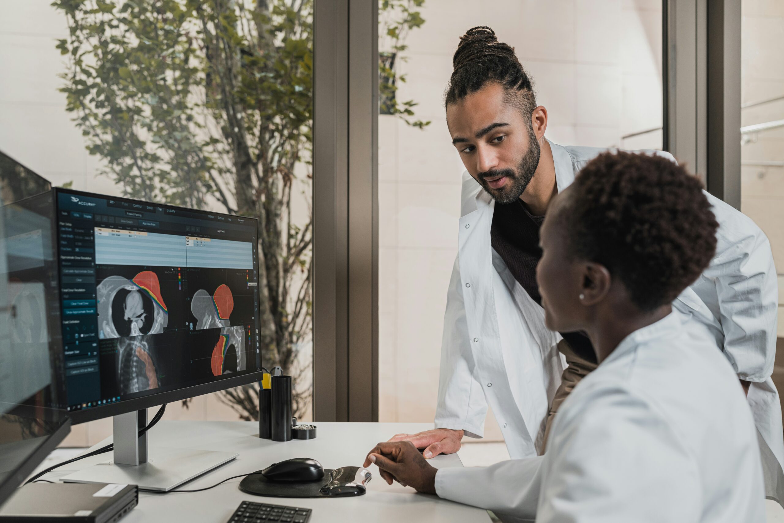 Two doctors in medical attire engaged in a discussion while looking at a computer screen, collaborating on patient data or medical research.